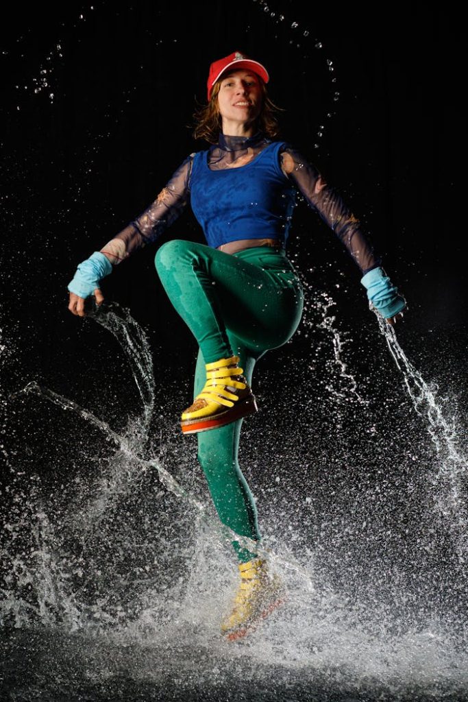 Low angle full length of slim active woman in bright outfit performing dance in splashing water