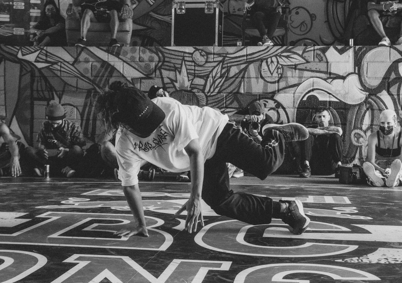 Black and white image of a street dancer performing in front of a graffiti wall.