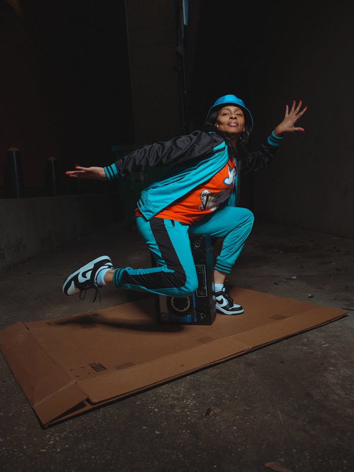 Dynamic street dancer in urban outfit striking a pose on cardboard in dimly lit alley.